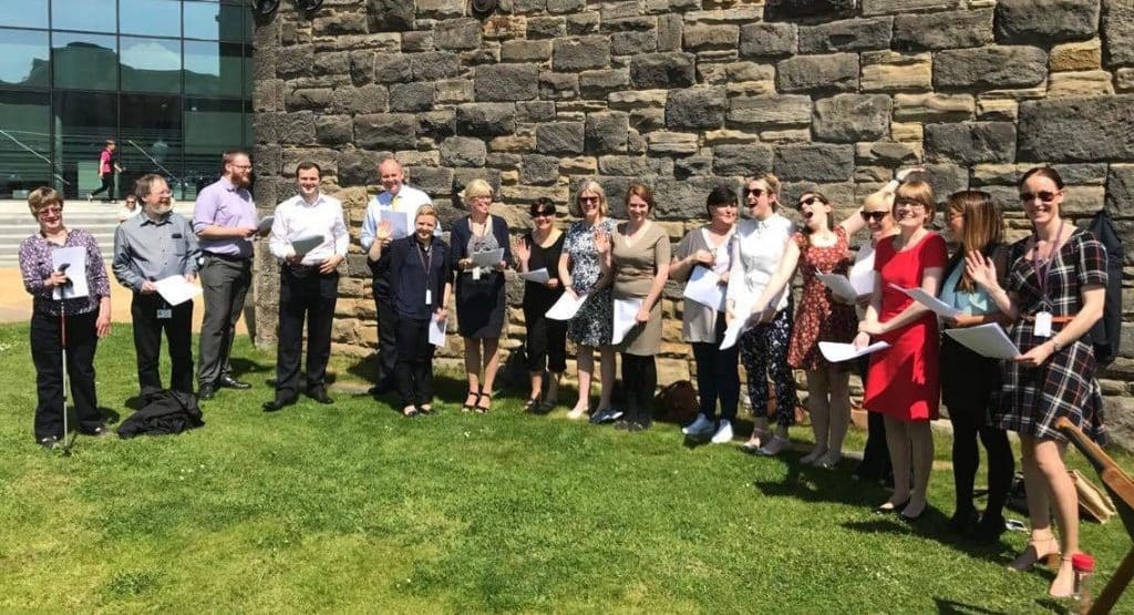 So Choir! Wellington Place Workplace Choir in Leeds singing outside on the grass and enjoying the sunshine
