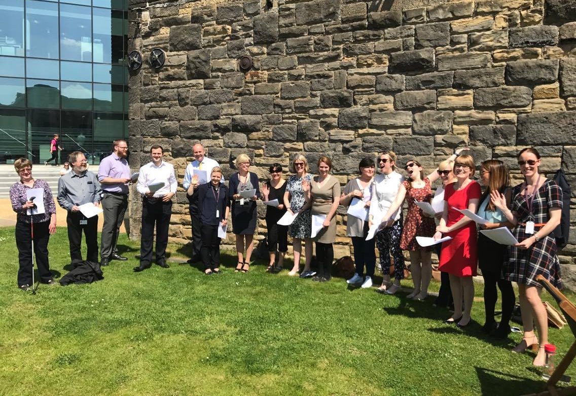 So Choir! Wellington Place Workplace Choir in Leeds singing outside on the grass and enjoying the sunshine