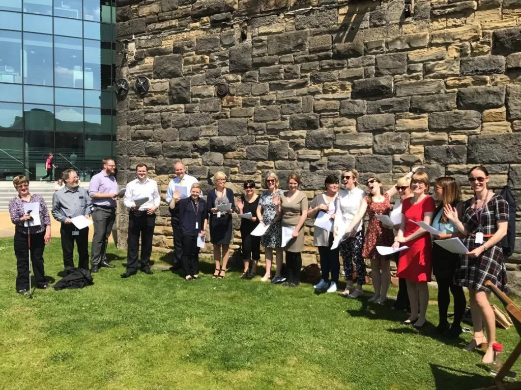 So Choir! Wellington Place Workplace Choir in Leeds singing outside on the grass and enjoying the sunshine